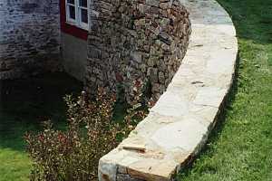 a curved natural stone wall on a grassy hill leading to an old red barn