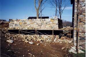 scaffolding around a natural stone wall. the ground is littered with stone pieces