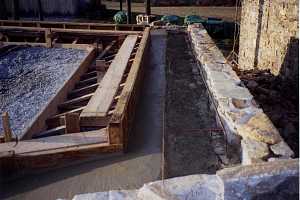 the top of a natural stone wall and the frame for a barn bridge that is going on top.