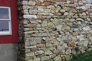 a natural stone wall attached to an old red barn