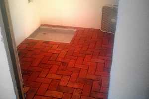 a red brick floor with a drain in the corner and a fan sitting on it