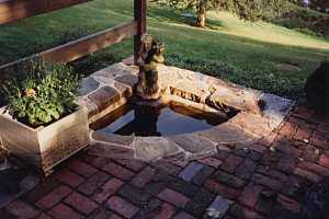 a natural stone pond surrounded by a planter and brick patio