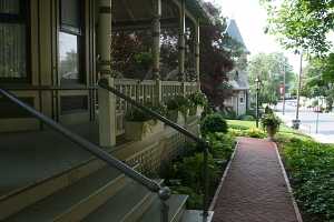 a porch and steps leading down to a brick walkway surrounded by gardens