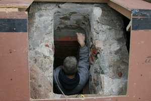 A man spreading fresh mortar on bricks inside a chimney flue