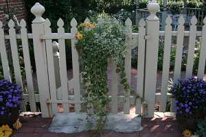 a white picket fence with a white concrete block under the door surrounded by a brick walkway