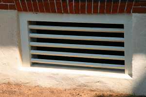 a painted wooden window grate in a concrete base of a brick home