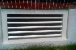 a painted wooden window grate in a concrete base of a brick home