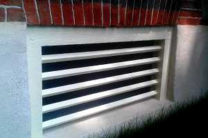 a painted wooden window grate in a concrete base of a brick home