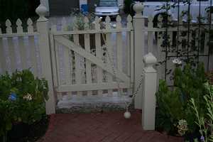 a white picket fence with a white concrete block under the door surrounded by a brick walkway