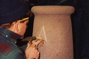 A stonemason carving letters into what will be a sundial pillar