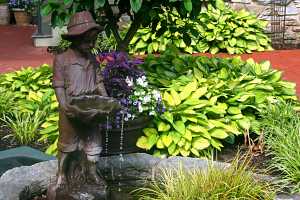 a small boy water fountain in a fish pond next to a decorative planter and shrubs