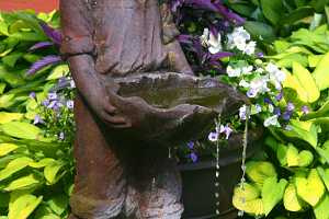 a small boy water fountain in a fish pond next to a decorative planter and in front of some green and yellow hostas