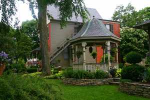 a gazebo in front of a brick home with a beautifully decorated landscape