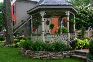 a gazebo surrounded by a beautiful landscape with shrubs, stone walls and other features