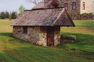 A restored stone spring house in front of a stone homee with red windows