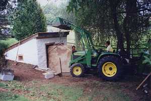 A green John Deere tractor moving a slab of stone into a restored spring house