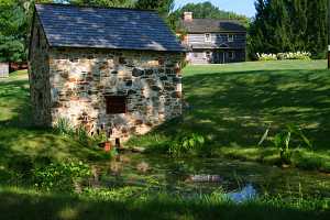 A fully restored stone spring house with a log cabin in the background