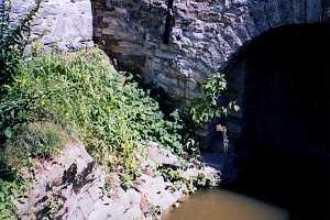 a stone retaining wall and stone archway near a bank above water