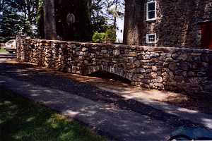 a rebuilt stone wall next to a driveway beside a stone home