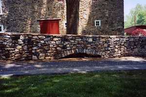 a rebuilt stone wall next to a driveway beside a stone home