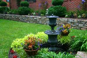 a fountain with a stone retaining wall and plants behind it