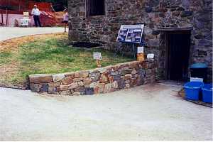  stone retaining wall leading into a stone building. a sign on the hill reads grist mill guided tours