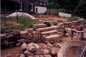 a stone wall and step installation in progress along with a backyard transformation