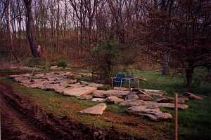 large stones waiting for a project in someones backyard. behind the stones are many trees