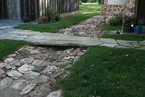 a large slab of stone acting as a bridge over a lower drainage ditch full of larger stones