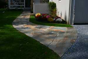 the full view of a newly installed stone sidewalk. mums and a white picket fence run along the garage next to the walkway.