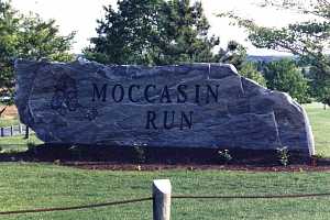 a large stone sign that reads moccasin run with a logo engraved in the stone and a flowerbed in front