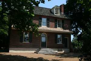 a brick home with green shutters and door featuring a newly installed concrete stairway and nautral stone steps on the right