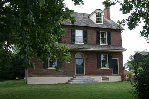 a brick home with green shutters and door featuring a newly installed concrete stairway and nautral stone steps on the right