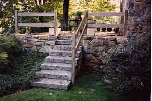 a stone wall and with stone steps leading up to a stone patio. a wood railing leads you up it.