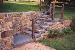 stone steps leading up to a landing, then leading up to a back yard. a wood railing leads you up it.