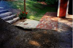 a brick walkway leading out of a home. stone steps run down a hill into a stone landing that connects to the brick walkway