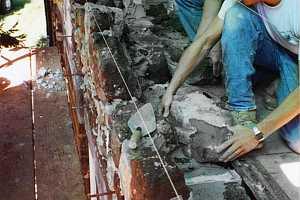 two men repairing a stone wall in a home