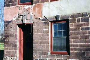 the end of a stone building with damaged stone caving in on the door frame