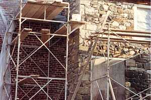 a man standing on scaffolding repairing a stone wall