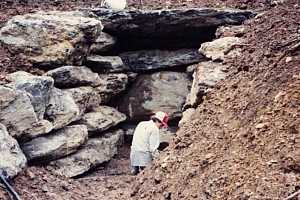 a man sitting in a large stone opening on a dirt hill - before