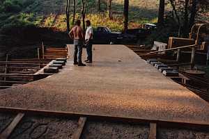 two men standing on a stone bridge with two trucks and a tractor downhill