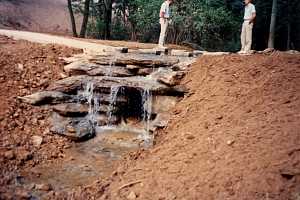 two men standing above a stone waterfall on a dirt hill