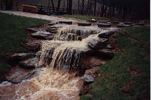 an overflowing stream running across the road and down a large stone waterfall