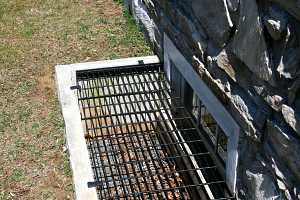 a black grate on a window well beneath a natural stone home