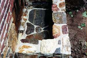 looking down in a natural stone window well with a drain in the middle